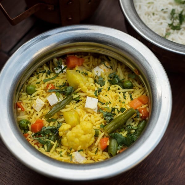 Close-up of Indian vegetable biryani with paneer, carrots, peas, and green beans in a metal bowl.