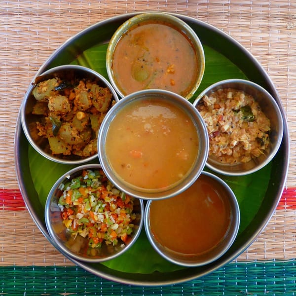 A traditional Indian thali with six small bowls of various curries and vegetable dishes on a banana leaf.