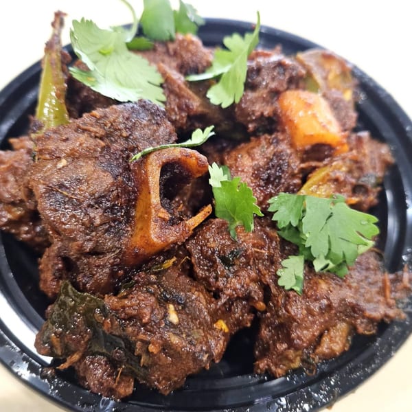 Close-up of Sai Bhavan's Indian goat curry, garnished with fresh cilantro and green chilies.
