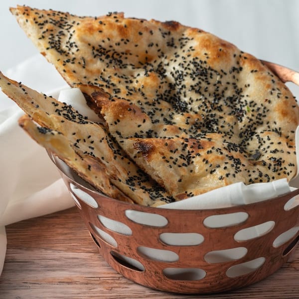 Indian naan bread, topped with black sesame seeds, in a copper basket with a white napkin.